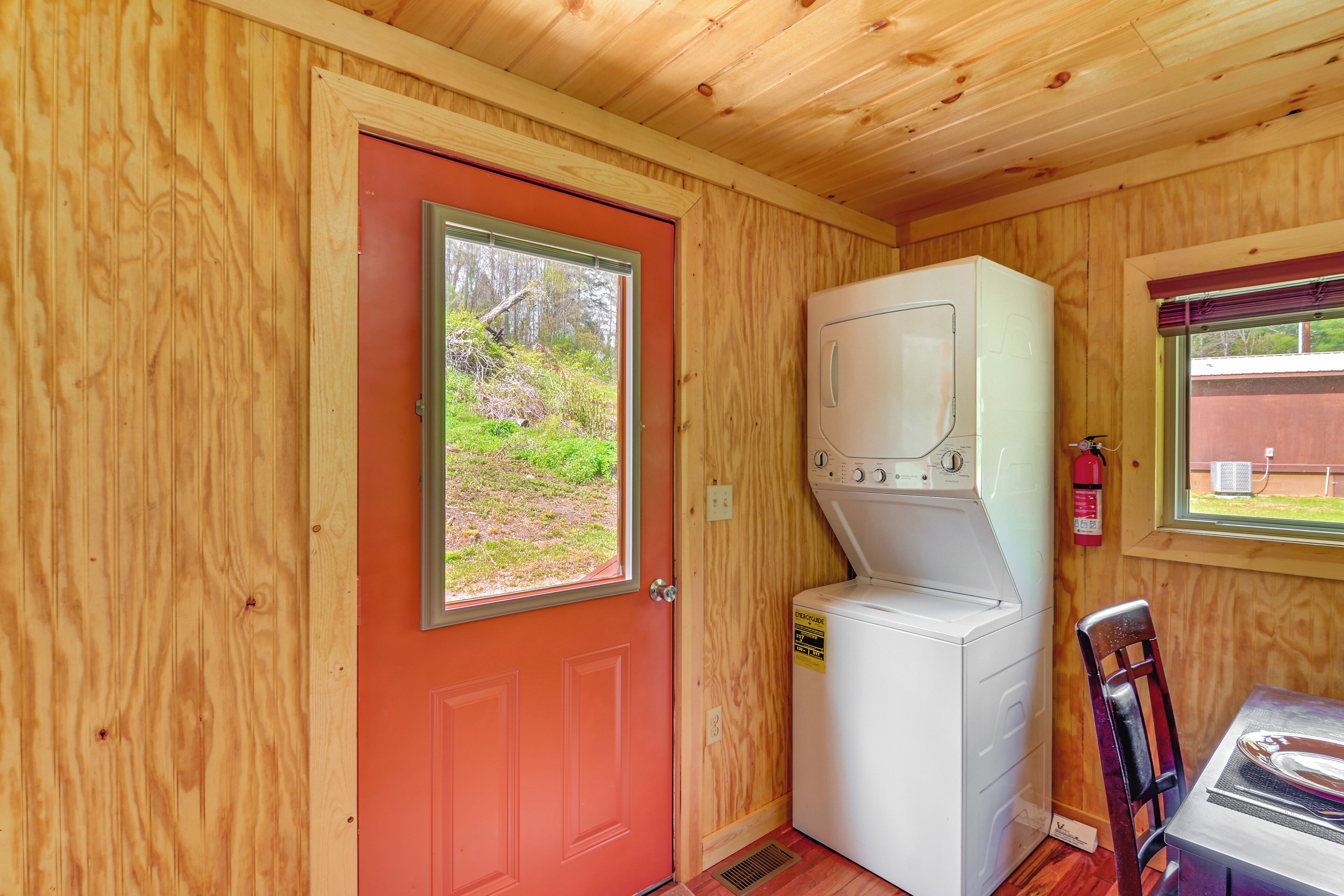 Habitación pequeña con puerta roja, lavadora y una mesa con una silla.