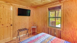A wooden cabin room with a bed, a chair, a television, and a window with a view of the outdoors.