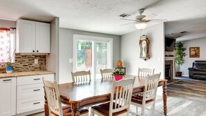 A dining room with a wooden table and chairs, a ceiling fan, and a view of the outdoors through a sliding glass door.