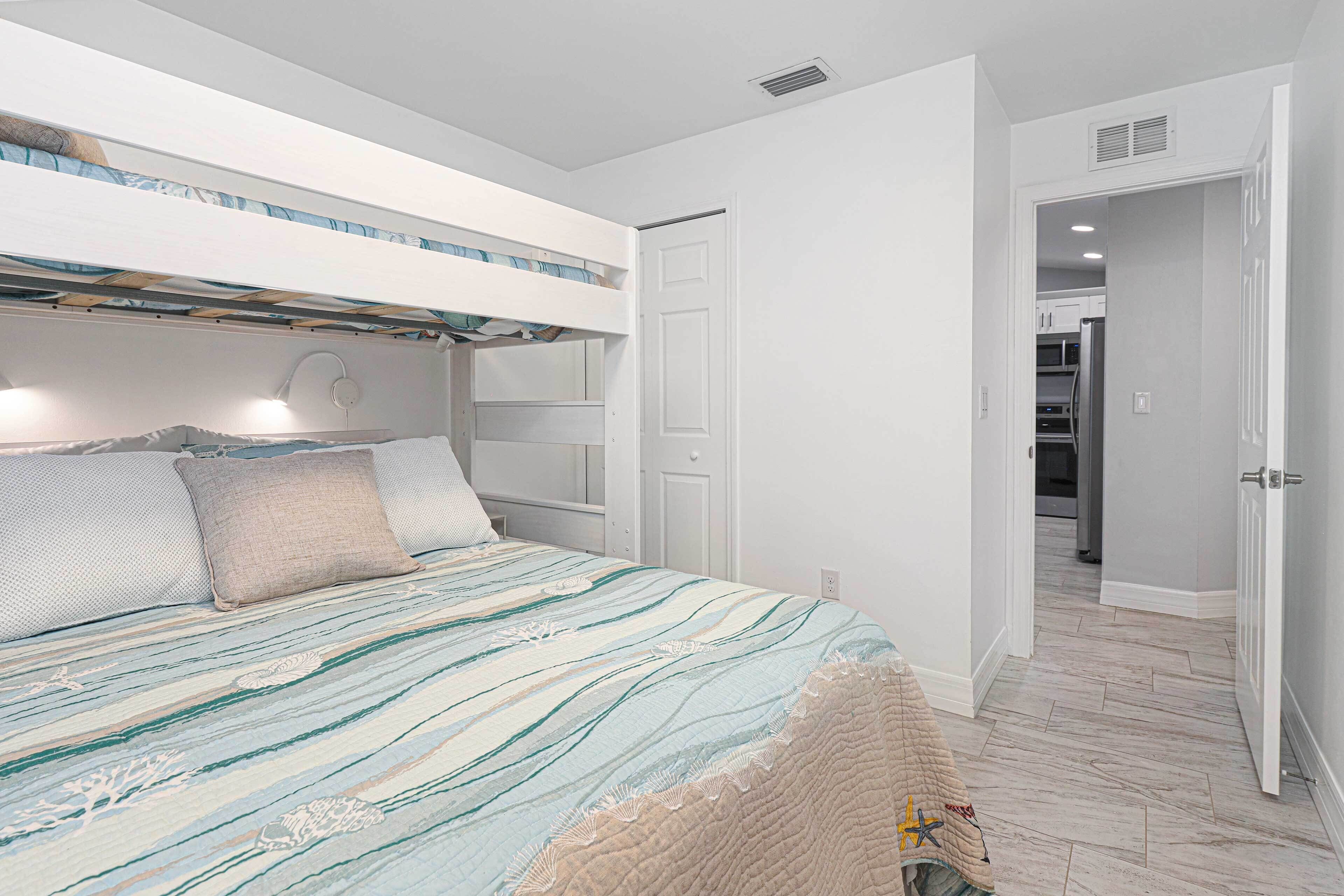 A bedroom with a bunk bed, a bedside table, and a door leading to a hallway.