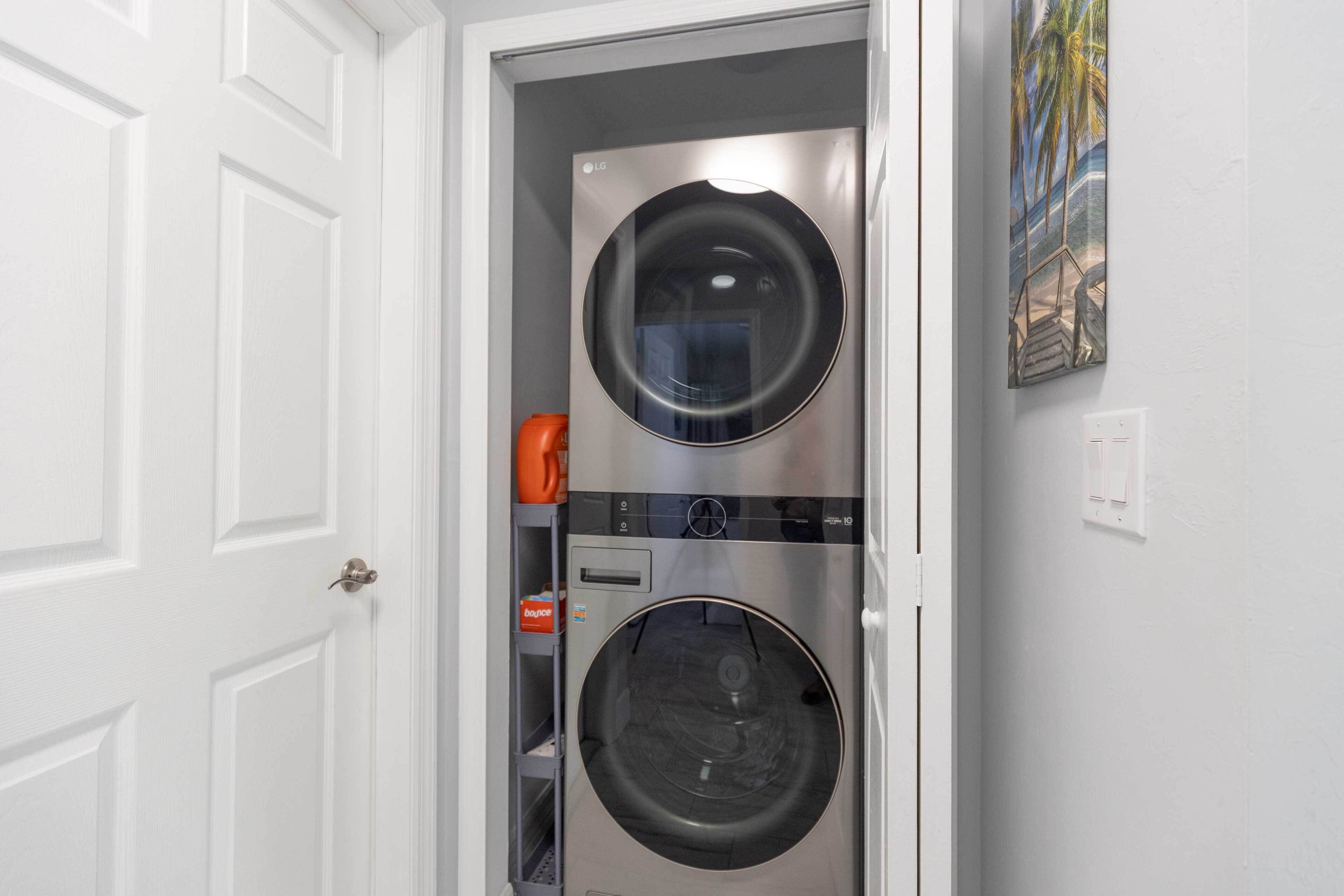 A compact laundry room with two stacked washing machines, a shelf with a bottle, and a painting on the wall.