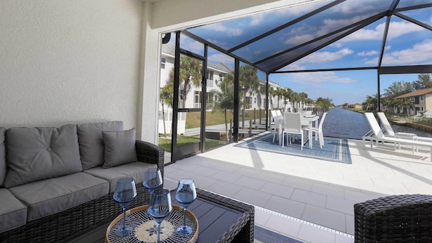 Un espacio de estar techado al aire libre con un sofá y una mesa, con vista a una piscina y una calle residencial.