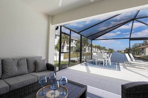 A covered outdoor seating area with a sofa and table, overlooking a pool and a residential street. - Cape Coral Duplex: Pool, Hot Tub, & Sunrise Views (Cape Coral)