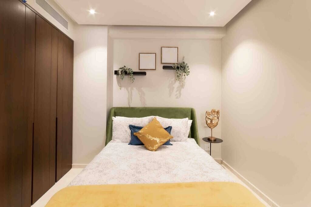 Een slaapkamer met een bed, een groen hoofdeinde, een nachtkastje met een decoratief object en een kledingkast.