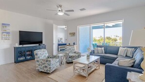 A modern living room with a flat-screen TV, patterned armchairs, a sofa, and a large window offering a view of the outdoors. - Ocean Oasis~  Pool Home, 35' Dock Near Coco Plum Beach! (Marathon)