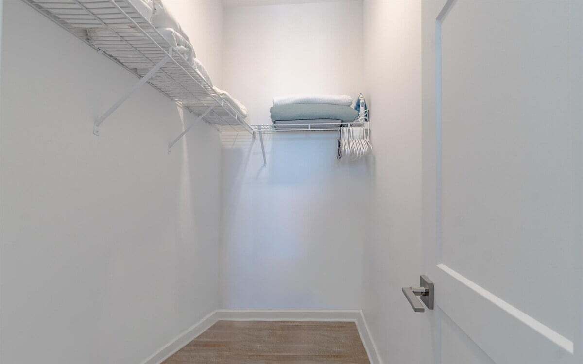 Un couloir étroit, avec une étagère métallique sur le côté gauche, un porte-serviettes avec une serviette sur le côté droit, et une porte au fond.