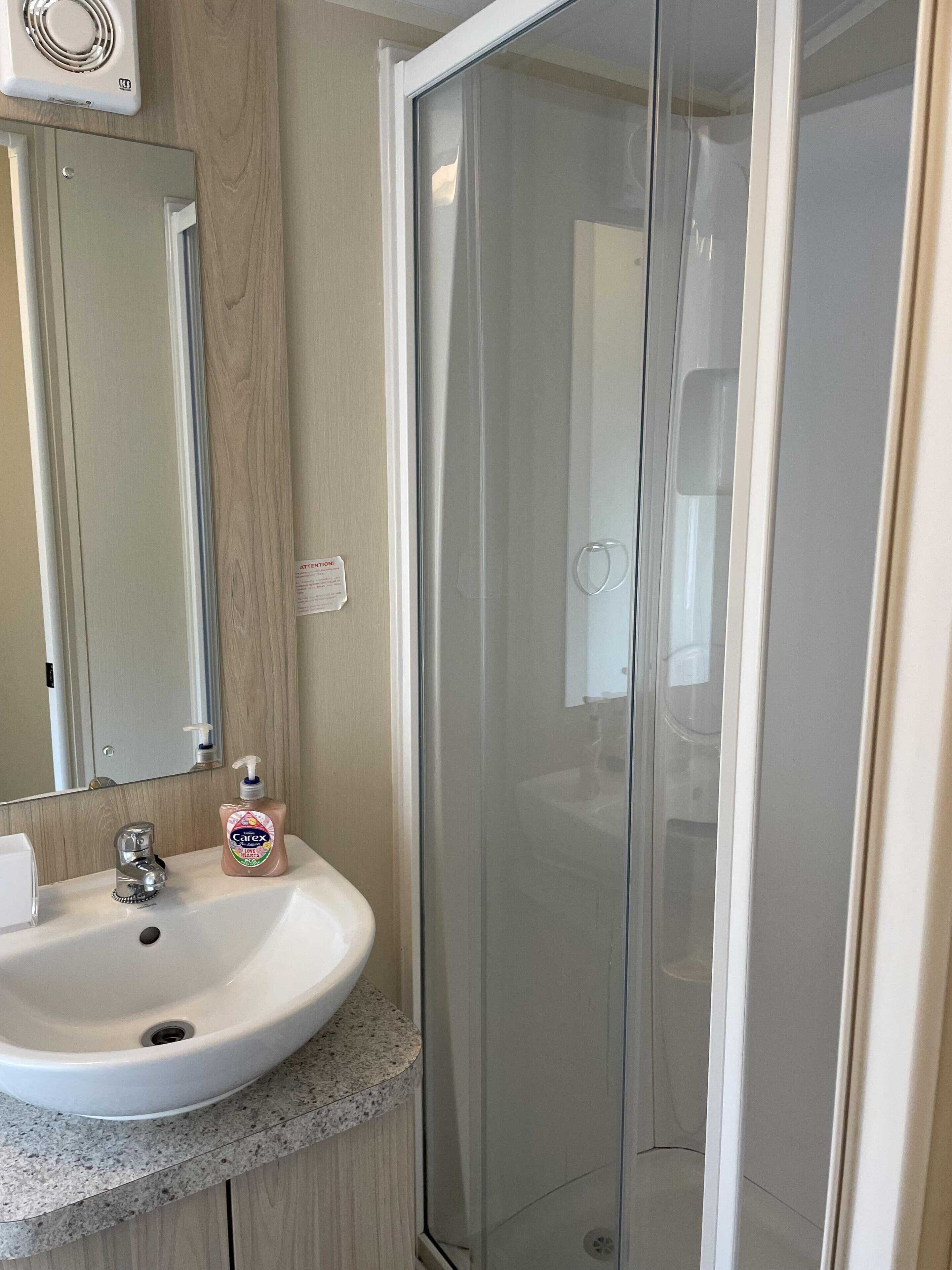 Une salle de bain avec un lavabo blanc, un miroir et une cabine de douche en verre.