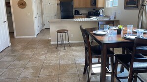 A kitchen with a central island, wooden cabinets, a refrigerator, and a dining area with chairs and a table set for two. - Lucky Seven Oasis by Mesquite Vacation Rentals with Community Pool and $510 in free daily activities (Mesquite)