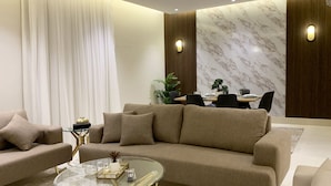 A modern living room with a beige sofa, a glass coffee table, and a dining area with a wooden table and chairs. - Kease Tawun B3-1 Royal touch  AG72 (Riyadh)