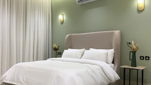 A neatly made bed with white bedding, a light-colored headboard, and a small table with a vase of flowers beside it. - Kease Tawun B3-1 Royal touch  AG72 (Riyadh)