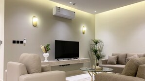 A modern living room with a flat-screen TV, beige sofas, a glass coffee table, and a potted plant. - Kease Tawun B3-1 Royal touch  AG72 (Riyadh)