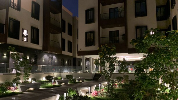 A modern building with multiple balconies and a well-lit courtyard with seating areas and greenery. - Kease Tawun B3-1 Royal touch  AG72 (Riyadh)