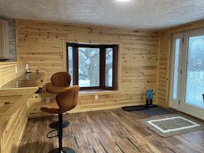 Un intérieur en bois avec un coin bar, une fenêtre donnant sur des arbres couverts de neige et une porte ornée de motifs en verre dépoli.