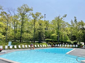 A swimming pool with clear water, surrounded by trees and white lounge chairs.