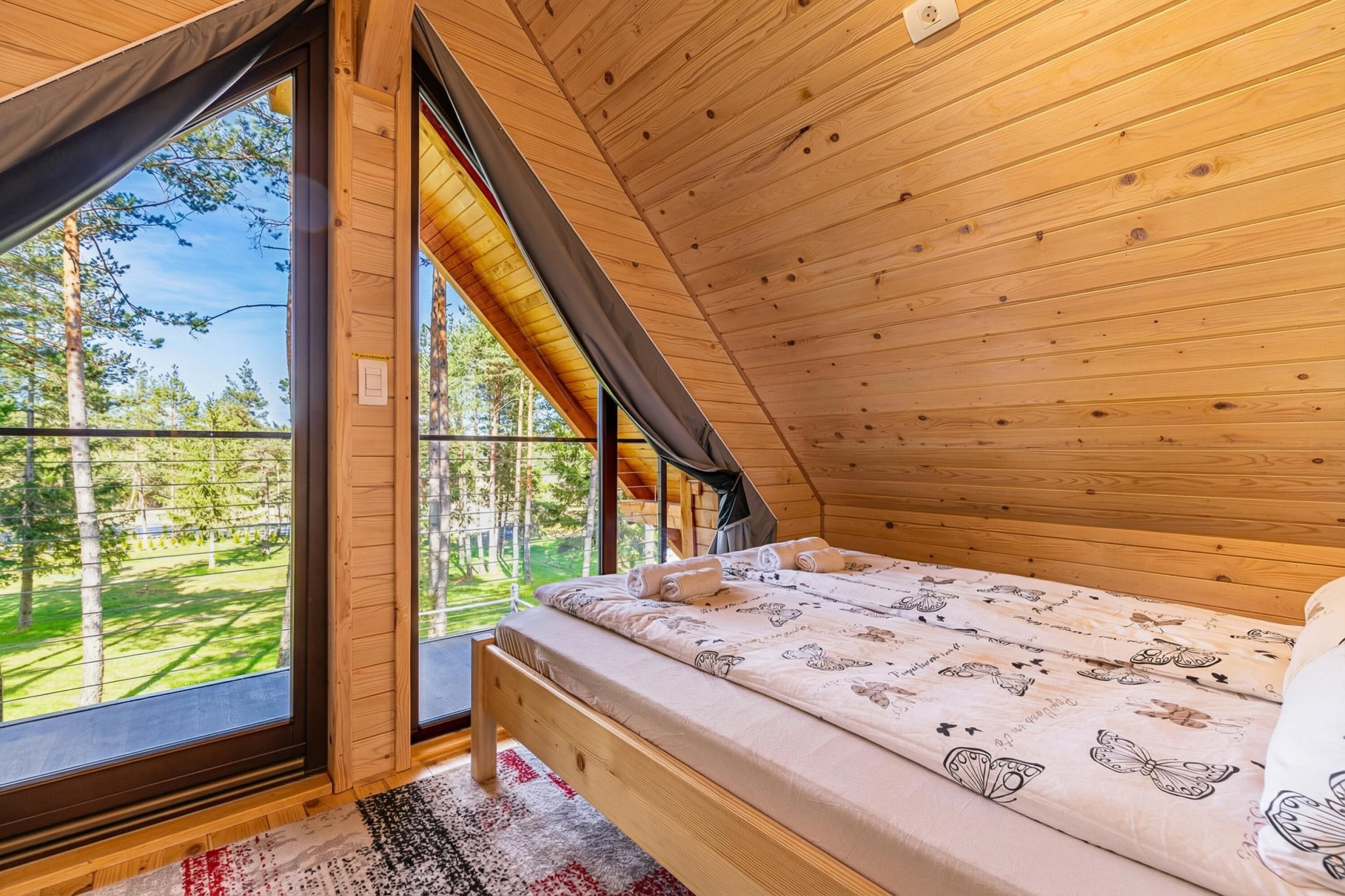 A bedroom with a large window, a bed with patterned bedding, and a view of a forest.