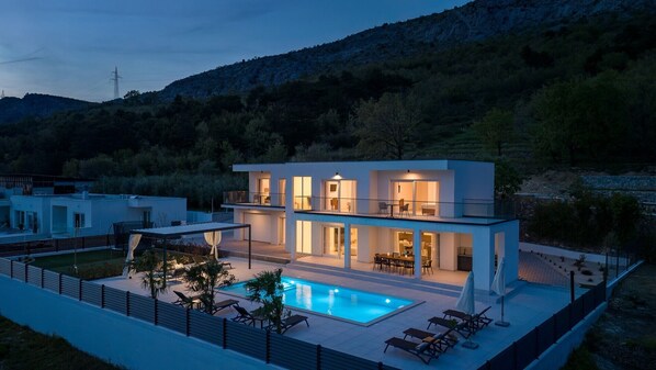 A modern two-story house with a swimming pool, surrounded by a fence and trees.