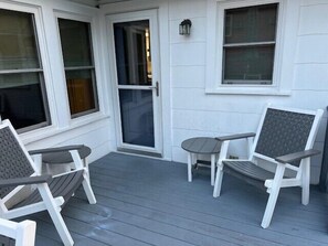 A covered porch with two white chairs and a small table, a sliding glass door, and a wall-mounted light fixture. - 5 bedroom oceanside house with a nice yard - walk to beach & town (Bethany Beach)