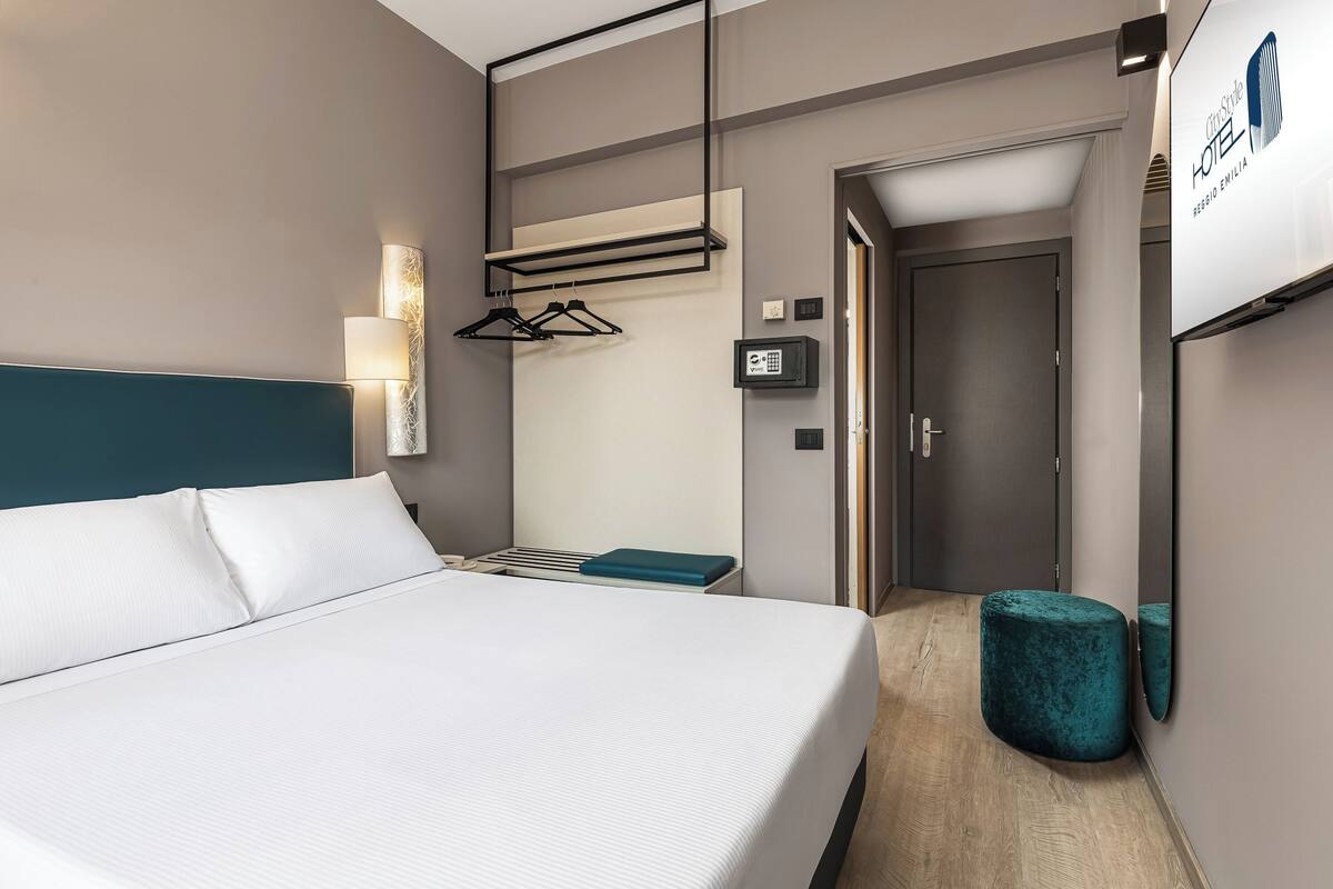 Ein modernes Hotelzimmer mit einem großen Bett, einem Nachttisch, einem an der Wand befestigten Fernseher und einer Tür zum Badezimmer.