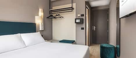 Una habitación de hotel moderna con una cama grande, una mesita de noche, un televisor montado en la pared y una puerta que da al baño.
