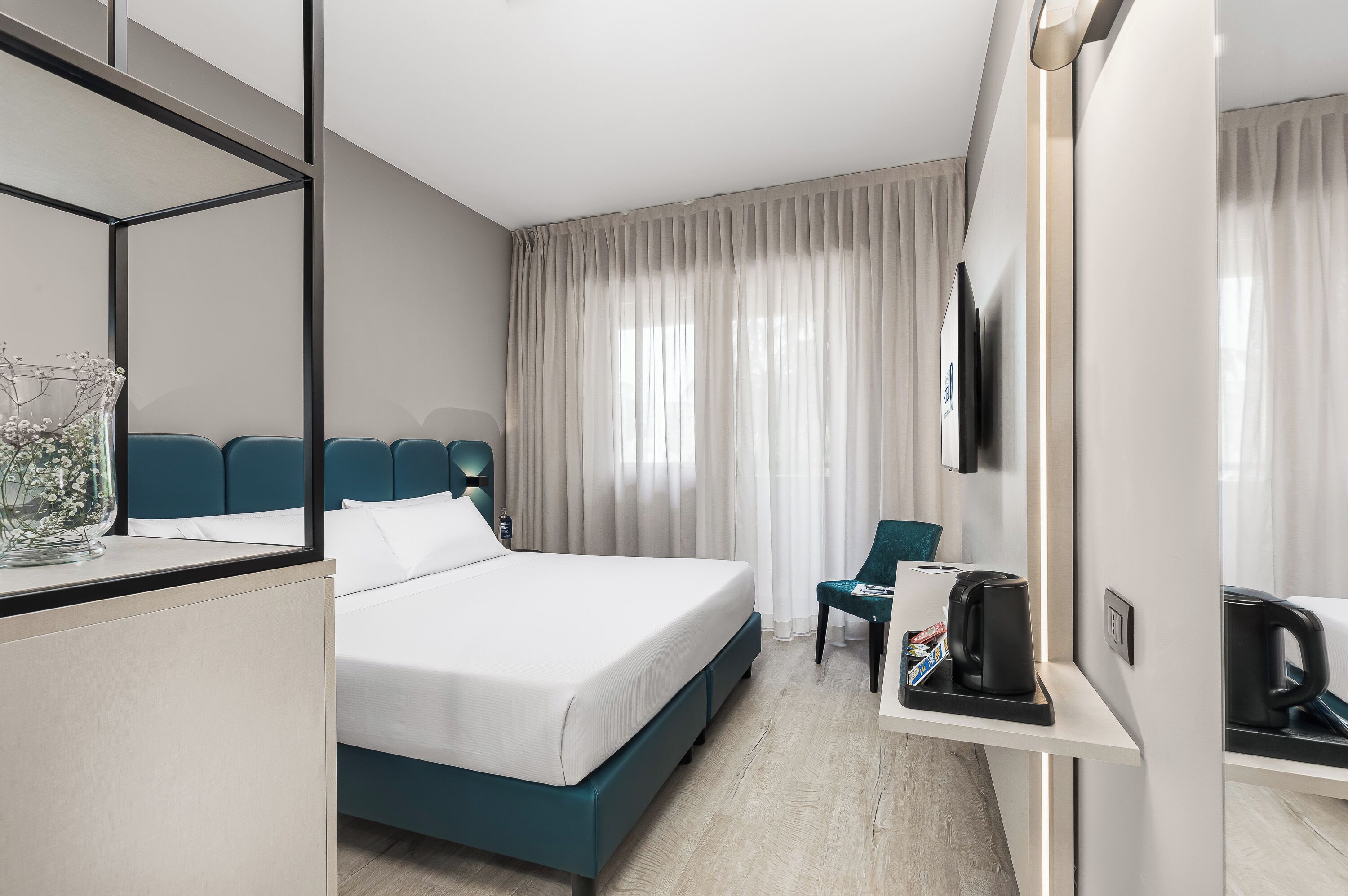 Ein modernes Hotelzimmer mit Bett, Sitzgelegenheit, einer Kaffeemaschine und einem Fernseher.