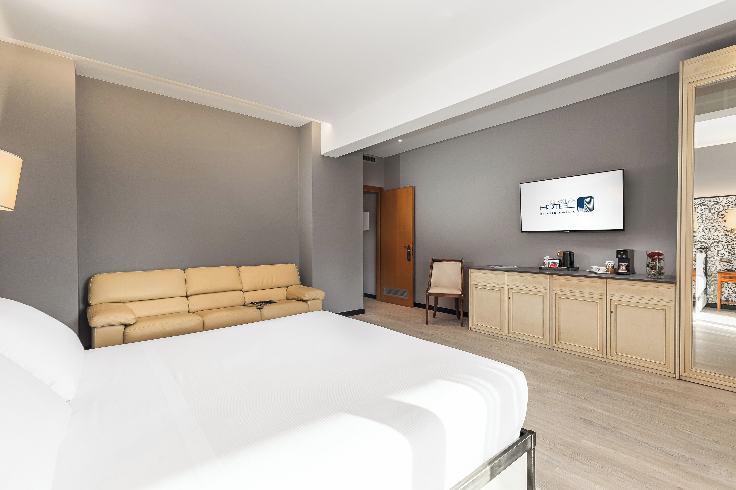 A modern hotel room with a large bed, a sofa, a television, and a minibar.
