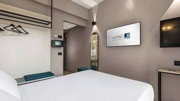 Quarto de hotel moderno com uma cama grande, televisão presa à parede e um espelho.
