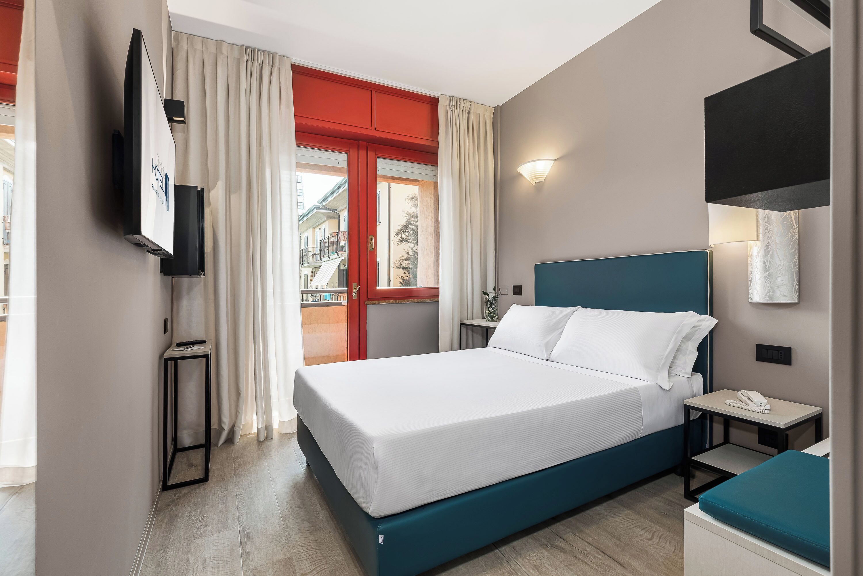 A hotel room with a bed, bedside table, and a TV mounted on the wall.