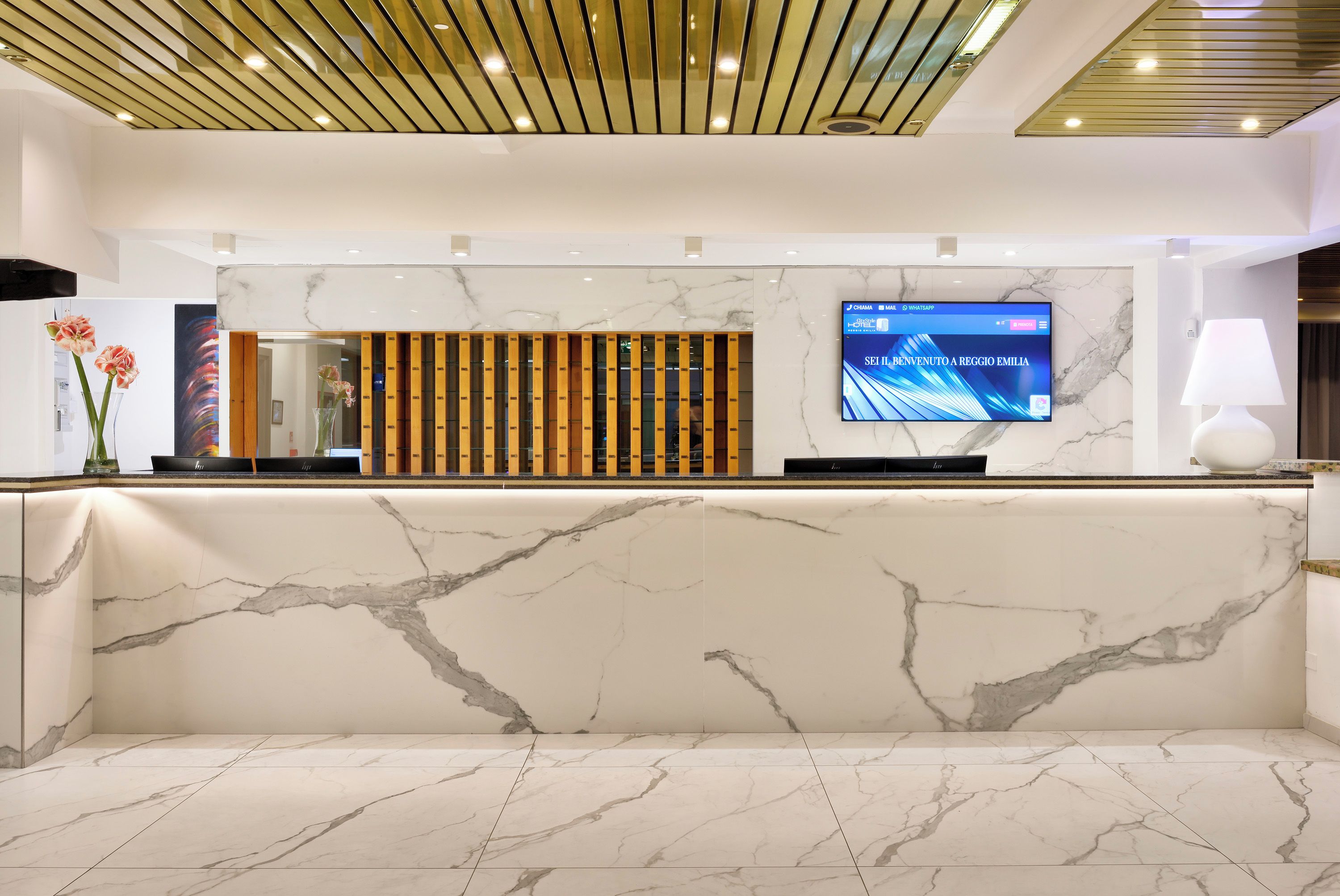 A reception area with a marble reception desk, a digital screen displaying a welcome message, and a modern ceiling design.