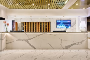 A reception area with a marble reception desk, a digital screen displaying a welcome message, and a modern ceiling design.