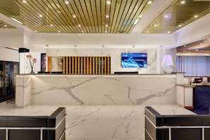 Ein Hotel-Empfangsbereich mit einem Marmor-Empfangstresen, einem digitalen Bildschirm und einem modernen Deckengestaltungsmerkmal.
