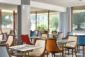 Ein Restaurant mit mehreren Tischen und Stühlen, großen Fenstern und Blick auf Grünflächen.
