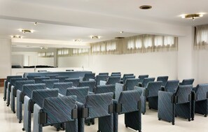 Un salón de conferencias con filas de sillas, una mesa grande y un espejo en la pared.