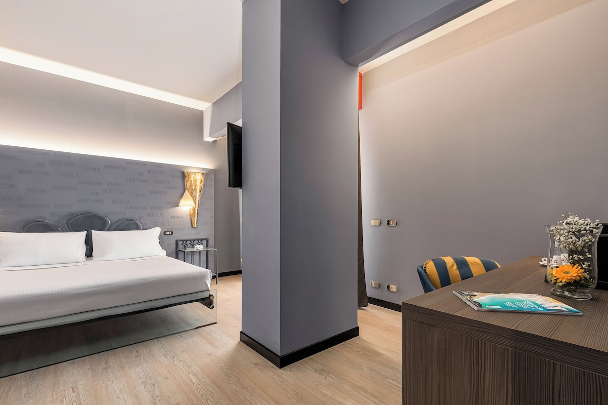 Una habitación de hotel moderna con una cama, mesita de noche, lámpara y un escritorio con un florero.