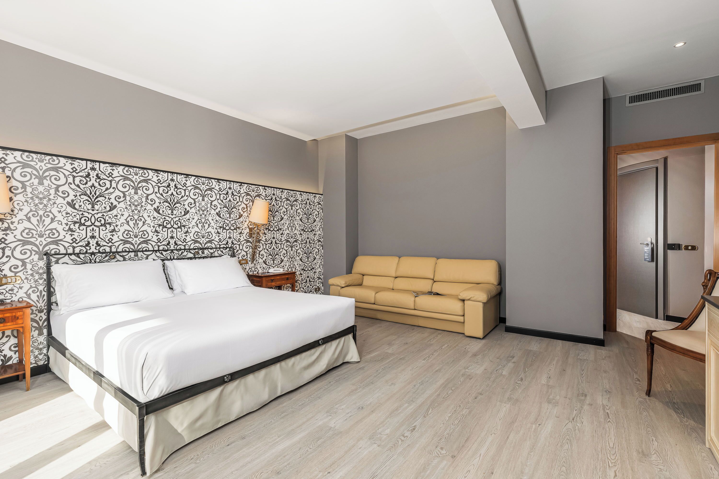 Een slaapkamer met een bed, een sofa, een nachtkastje en een muur met een patroon.