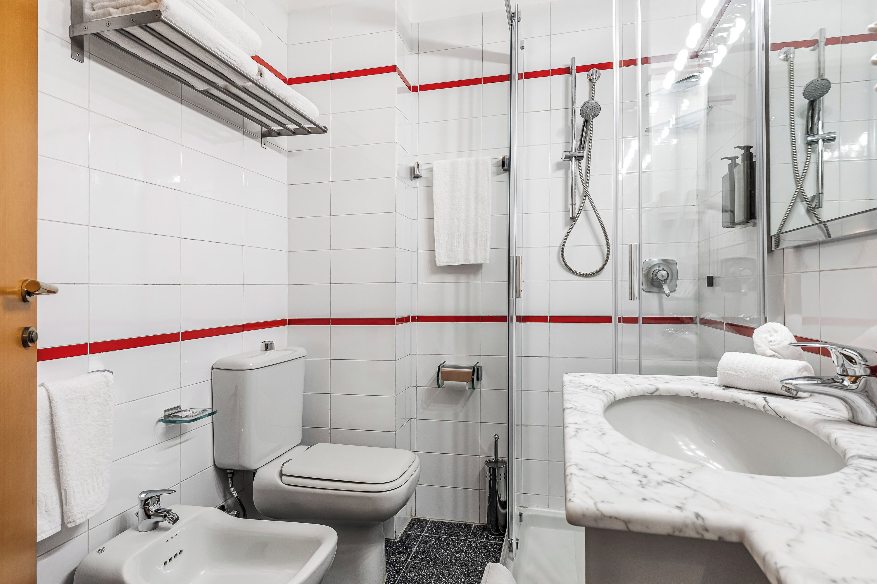 A modern bathroom with a toilet, bidet, sink, and glass-enclosed shower area.