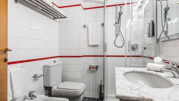 A modern bathroom with a toilet, bidet, sink, and glass-enclosed shower area.