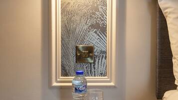 A nightstand with a water bottle and a glass, a wall-mounted light, and a switch.