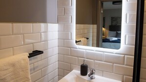 Un baño con azulejos blancos tipo metro, un lavamanos blanco, un espejo y un perchero para toallas.