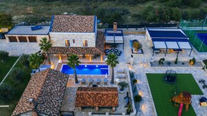 Une grande maison avec une piscine, un espace salon extérieur et un court de tennis.