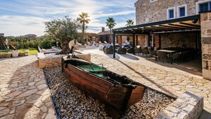 Une terrasse en pierre avec un bateau, des sièges d’extérieur et un bâtiment aux murs et aux fenêtres en pierre.