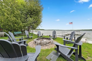 Et siddeområde ved søen med Adirondack-stole, en bålplads og et amerikansk flag.