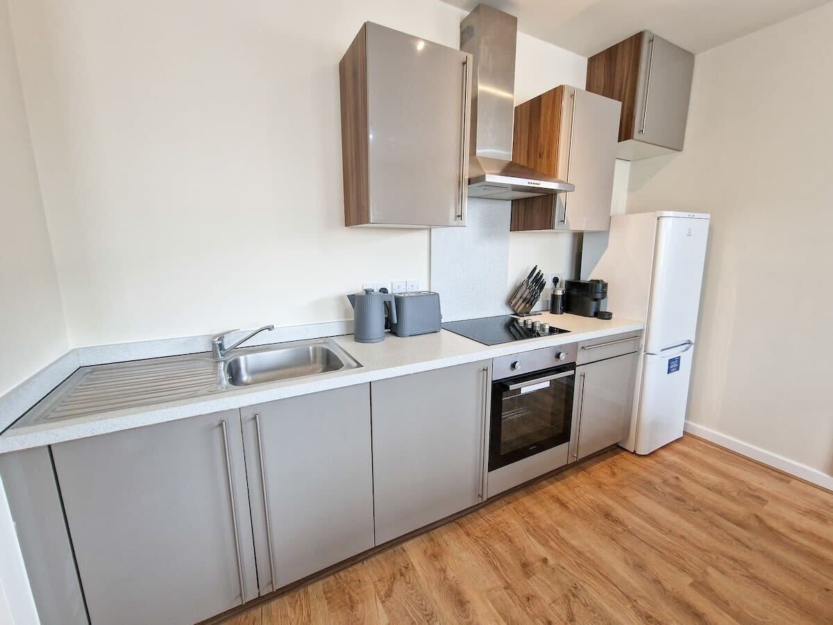 A modern kitchen with grey cabinets, a stainless steel range hood, a built-in oven, and a white refrigerator.
