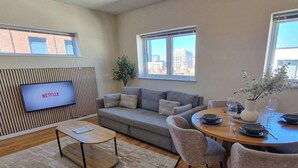 A modern living room with a grey sofa, a coffee table, a dining table set for four, and a TV mounted on a wooden panel wall. - 2 Bed City Centre Flat | Free Parking (Manchester)