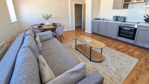 A modern living room with a sofa, a dining table with chairs, a kitchen area with cabinets and appliances, and a ceiling fan. - 2 Bed City Centre Flat | Free Parking (Manchester)