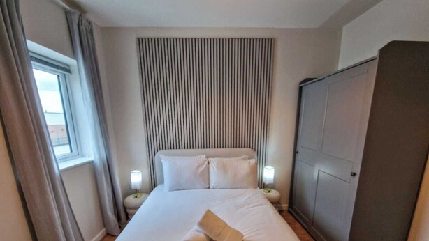 A hotel room with a bed, a wardrobe, a window with curtains, and bedside lamps. - 2 Bed City Centre Flat | Free Parking (Manchester)