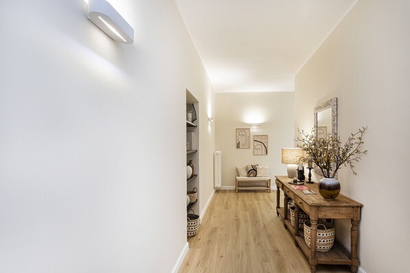 A hallway with a wooden floor, a wooden console table with baskets, a lamp, and wall art.