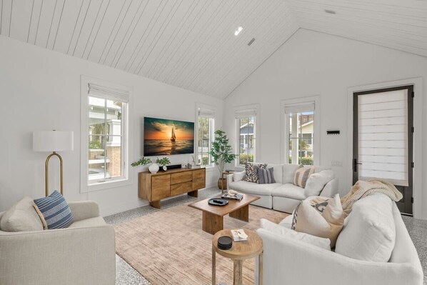 A spacious living room with a high ceiling, a large TV, a wooden cabinet, and a cozy seating area with a sofa and armchairs.