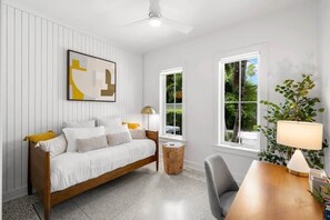 A modern bedroom with a wooden bed, a side table, a lamp, and a window with a view of greenery.