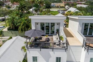 A modern house with a rooftop patio featuring outdoor furniture, a large umbrella, and a view of the surrounding neighborhood.