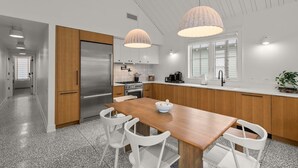 A modern kitchen with a wooden table, white chairs, a stainless steel refrigerator, and pendant lights.